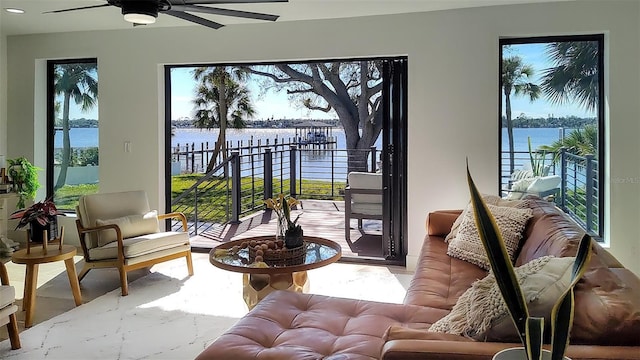 living area featuring a ceiling fan, a water view, and a wealth of natural light