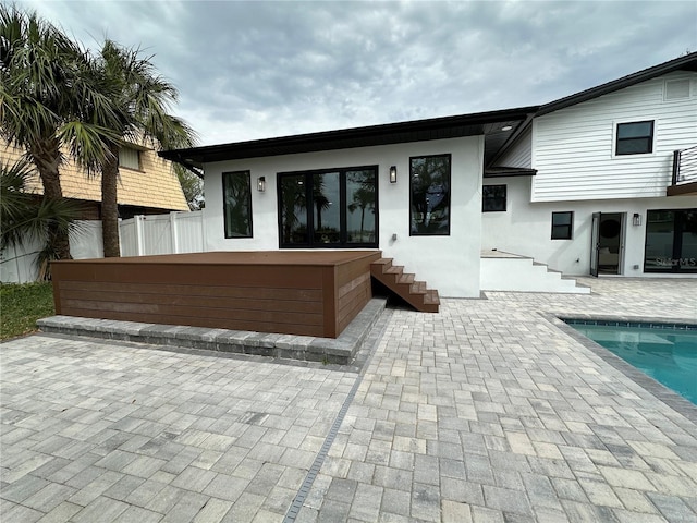 rear view of property with a patio area, stucco siding, an outdoor pool, and fence