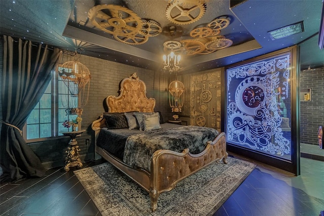 bedroom with a tray ceiling, visible vents, brick wall, and wood finished floors