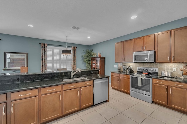 kitchen featuring visible vents, brown cabinetry, decorative backsplash, stainless steel appliances, and a sink