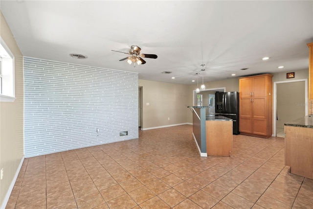 kitchen with light tile patterned floors, visible vents, black fridge with ice dispenser, dark stone countertops, and brick wall