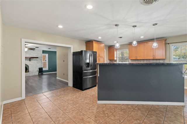 kitchen with light tile patterned floors, a large fireplace, black fridge with ice dispenser, dark stone counters, and pendant lighting