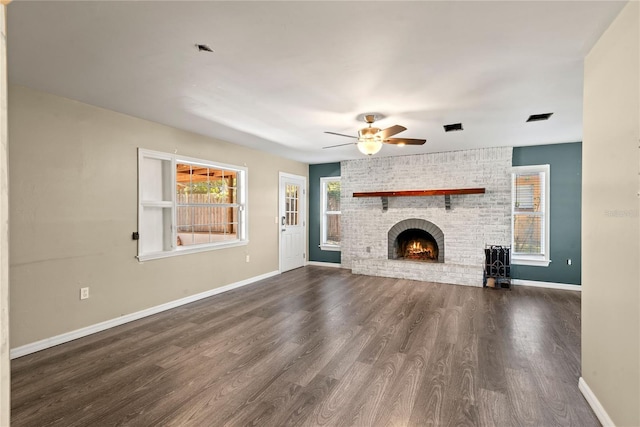 unfurnished living room featuring a brick fireplace, baseboards, dark wood finished floors, and a ceiling fan