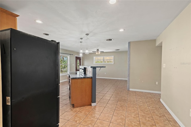 kitchen with light tile patterned floors, dark countertops, freestanding refrigerator, ceiling fan, and baseboards