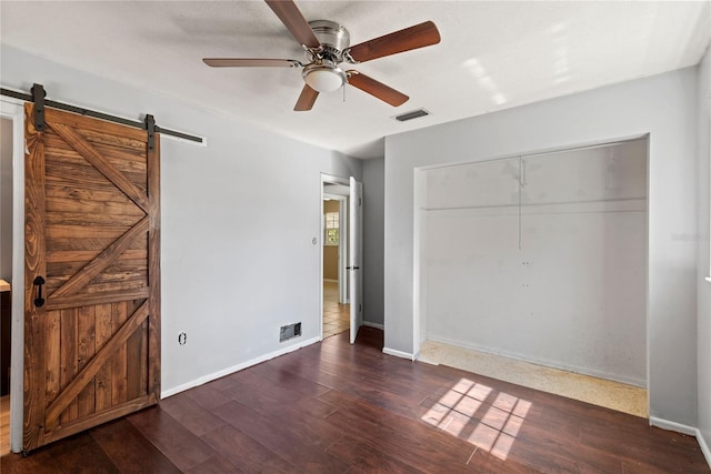 unfurnished bedroom with a barn door, wood finished floors, visible vents, baseboards, and a closet