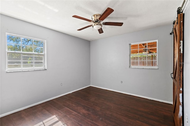 empty room featuring a wealth of natural light, wood finished floors, ceiling fan, and a barn door