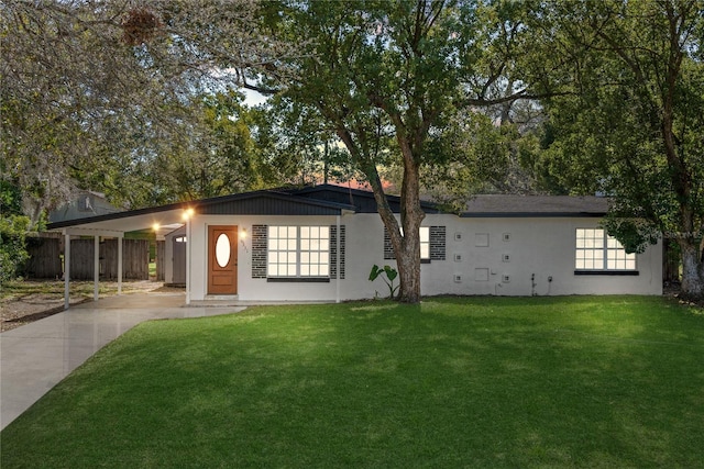 mid-century home featuring an attached carport, concrete driveway, stucco siding, and a front yard