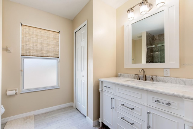 bathroom with toilet, wood finished floors, vanity, baseboards, and tiled shower