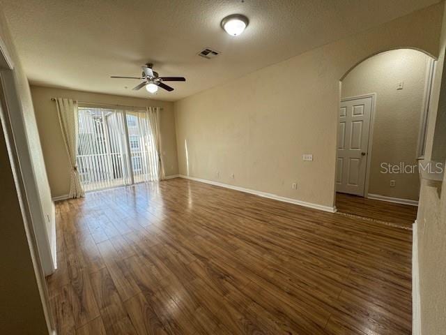 empty room with visible vents, baseboards, ceiling fan, wood finished floors, and arched walkways
