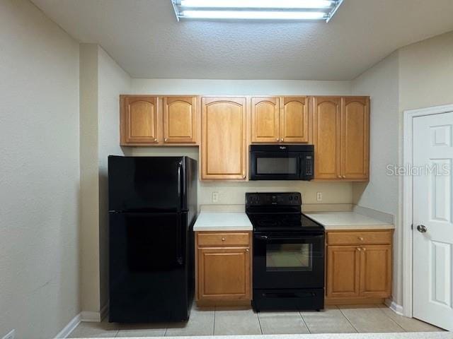 kitchen featuring light tile patterned floors, baseboards, black appliances, and light countertops