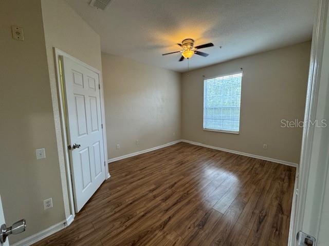 empty room featuring visible vents, baseboards, ceiling fan, and dark wood-style flooring