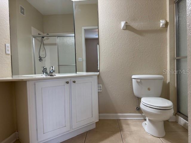 bathroom featuring tile patterned flooring, visible vents, a shower stall, toilet, and vanity