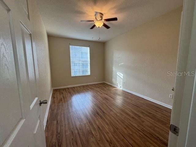 spare room with baseboards, dark wood-type flooring, a ceiling fan, and a textured ceiling