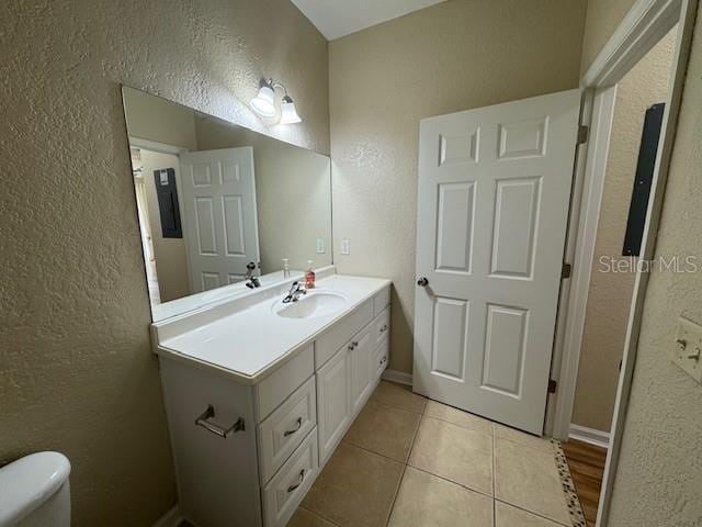 half bathroom with vanity, baseboards, tile patterned floors, toilet, and a textured wall