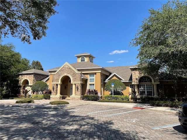 view of front facade with stone siding, stucco siding, roof with shingles, and uncovered parking