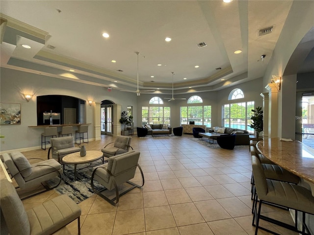 living area featuring a tray ceiling, light tile patterned flooring, crown molding, and visible vents