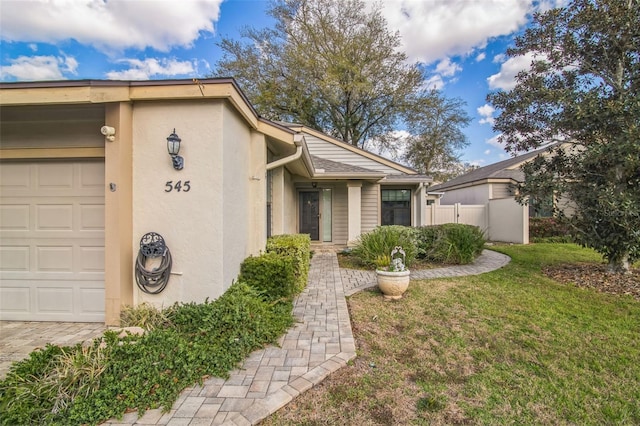 view of front facade with a garage, fence, a front lawn, and stucco siding