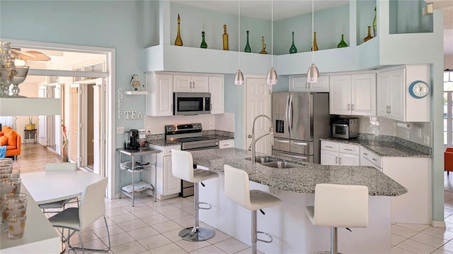 kitchen with a breakfast bar, light tile patterned flooring, white cabinets, stainless steel appliances, and a sink