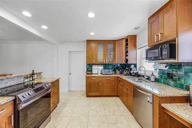 kitchen featuring light stone counters, stainless steel appliances, tasteful backsplash, brown cabinetry, and a sink