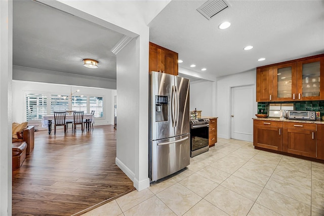 kitchen with light stone counters, visible vents, appliances with stainless steel finishes, brown cabinetry, and glass insert cabinets