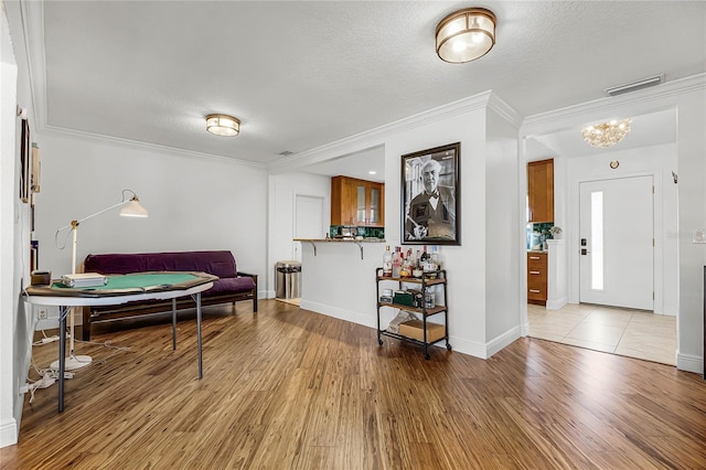 entryway with baseboards, visible vents, ornamental molding, wood finished floors, and a textured ceiling