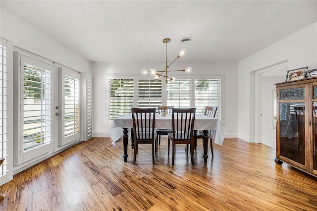 dining area featuring a chandelier, a textured ceiling, visible vents, baseboards, and light wood-type flooring