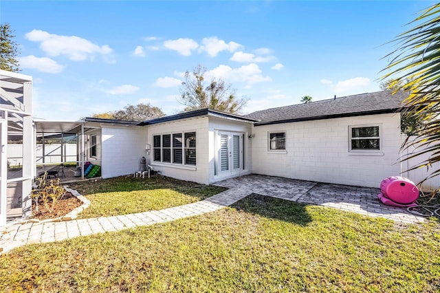 rear view of house featuring a patio area, a lawn, concrete block siding, and a lanai