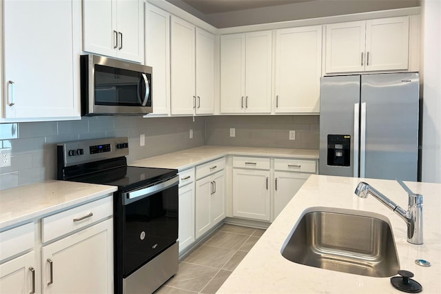 kitchen featuring appliances with stainless steel finishes, a sink, white cabinetry, backsplash, and light tile patterned flooring