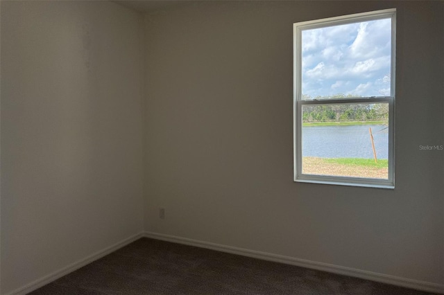 spare room with a water view, baseboards, and dark carpet