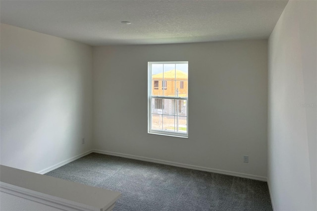 spare room with dark carpet, a textured ceiling, and baseboards