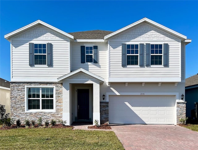 view of front facade with decorative driveway, roof with shingles, an attached garage, a front yard, and stone siding