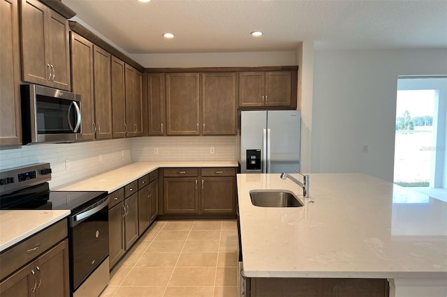 kitchen with light tile patterned floors, decorative backsplash, appliances with stainless steel finishes, a sink, and an island with sink