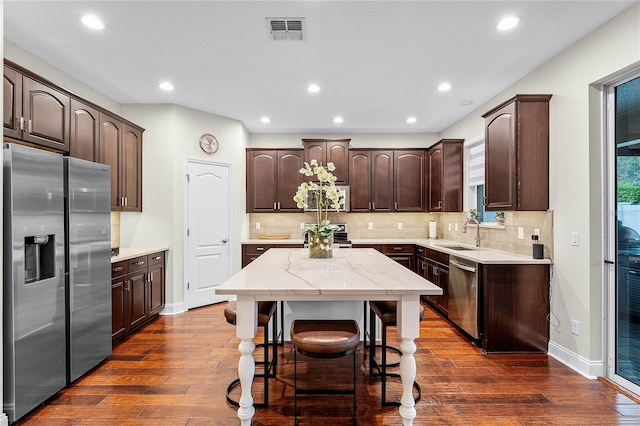 kitchen featuring dark brown cabinetry, decorative backsplash, appliances with stainless steel finishes, dark wood-style floors, and a sink