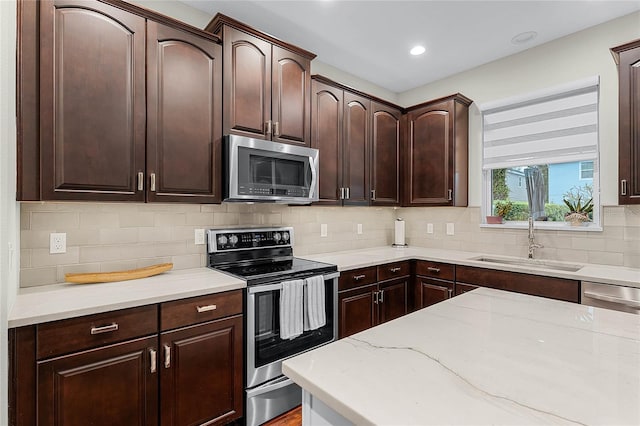 kitchen featuring light stone countertops, a sink, dark brown cabinets, appliances with stainless steel finishes, and backsplash