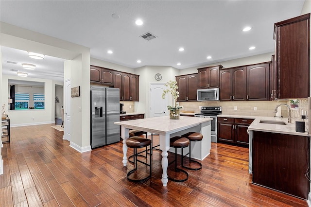 kitchen with visible vents, a sink, stainless steel appliances, dark brown cabinets, and a center island