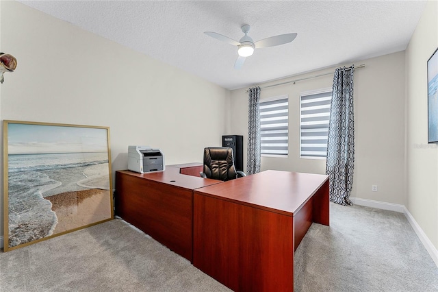 office space featuring baseboards, light colored carpet, a ceiling fan, and a textured ceiling