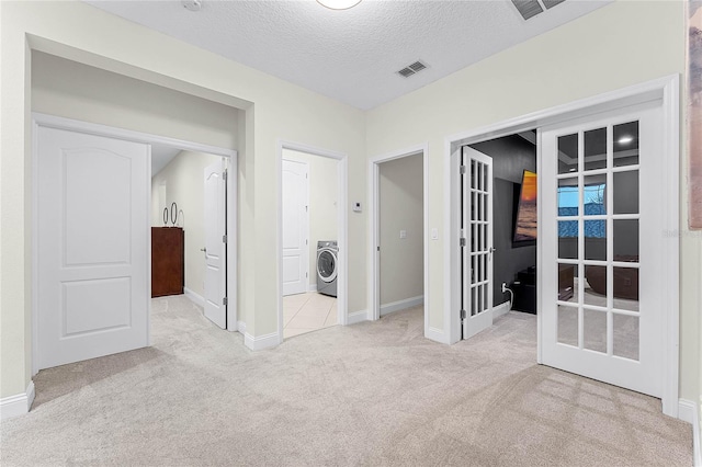 unfurnished bedroom featuring visible vents, a textured ceiling, french doors, carpet floors, and washer / dryer