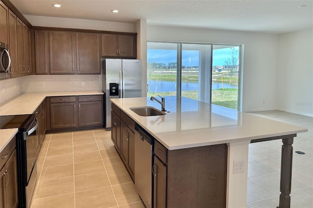 kitchen with light tile patterned floors, stainless steel appliances, decorative backsplash, a sink, and an island with sink