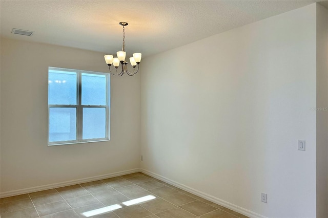 spare room featuring visible vents, a notable chandelier, a textured ceiling, and baseboards