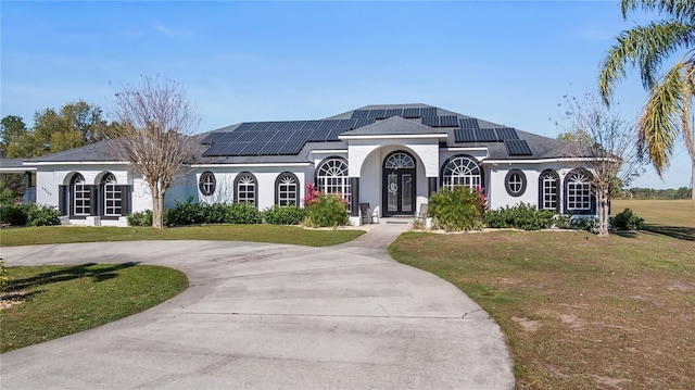 view of front of house featuring stucco siding, curved driveway, solar panels, and a front lawn