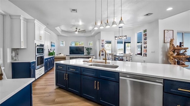 kitchen with visible vents, blue cabinetry, a tray ceiling, a sink, and stainless steel appliances