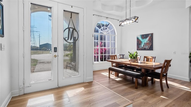 dining room featuring light wood finished floors, french doors, baseboards, and an inviting chandelier