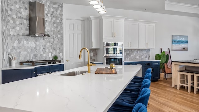 kitchen featuring wall chimney range hood, blue cabinetry, stainless steel appliances, and a sink