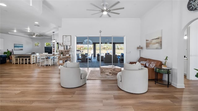 living room with arched walkways, wood finished floors, a ceiling fan, and crown molding