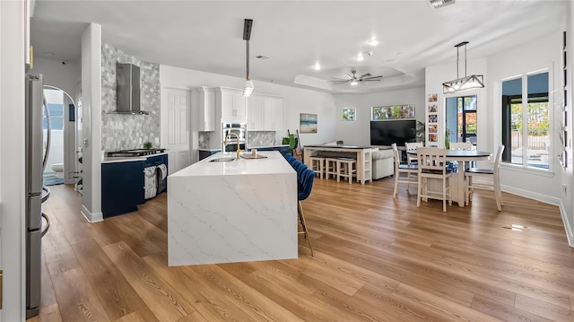 kitchen featuring wall chimney range hood, gas range oven, freestanding refrigerator, light wood finished floors, and ceiling fan