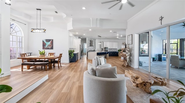 living room featuring baseboards, ornamental molding, ceiling fan with notable chandelier, light wood-style flooring, and a towering ceiling