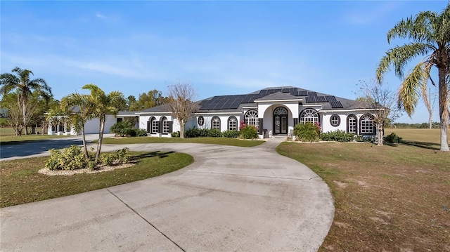 view of front of home featuring solar panels, a front yard, stucco siding, and curved driveway