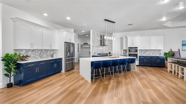 kitchen with wall chimney range hood, a kitchen bar, light countertops, stainless steel appliances, and blue cabinets