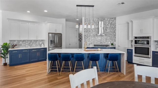 kitchen featuring wall chimney range hood, a sink, blue cabinetry, and appliances with stainless steel finishes