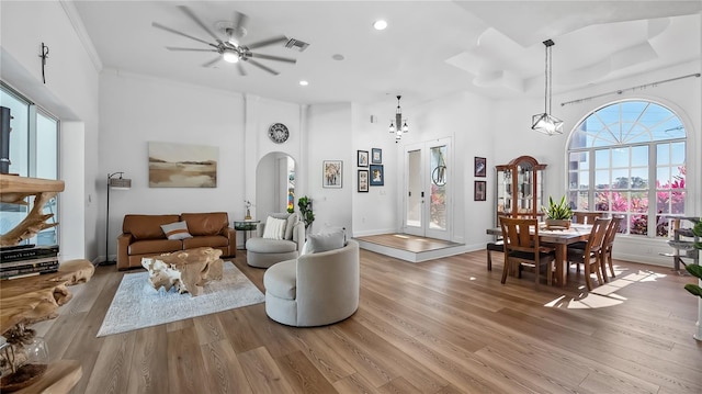 living room featuring arched walkways, light wood-type flooring, ceiling fan, visible vents, and a high ceiling
